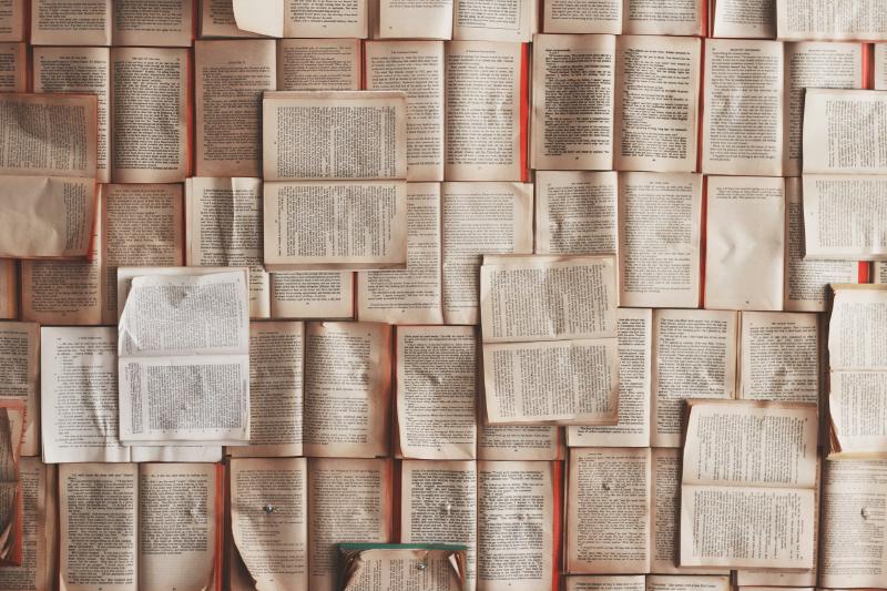 Foto: Ganz viele Bücher liegen übereinander. Vermutlich wurden sie mit Bolzen an eine Wand montiert? Das Bild lässt nur Vermutungen zu
