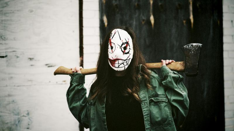 Foto: Eine Frau mit einer gruseligen Maske, die eine Axt hält.